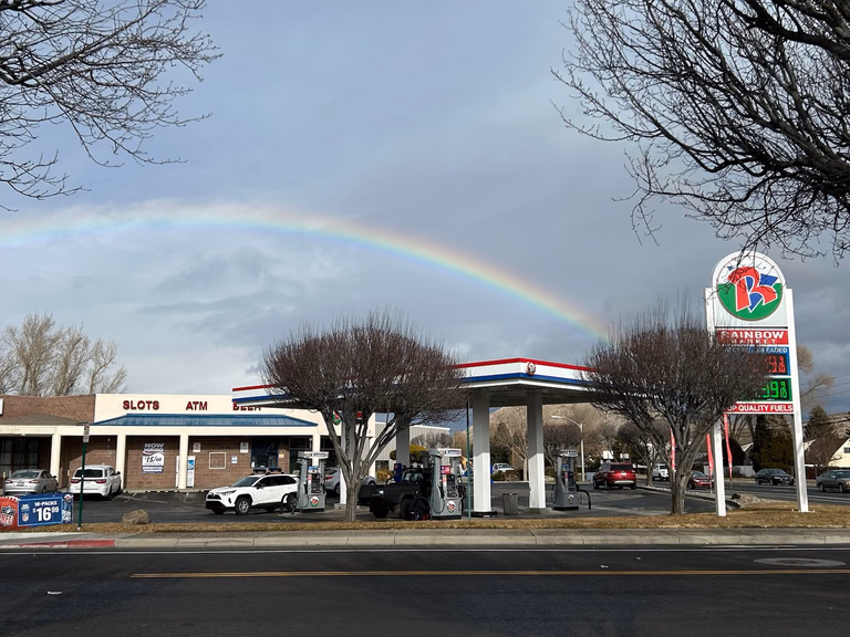 Convenience store storefront with fuel pumps and a rainbow overhead